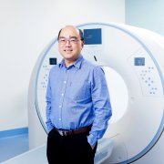 Dr Yu Ming Tang standing in front of an MRI Machine image request