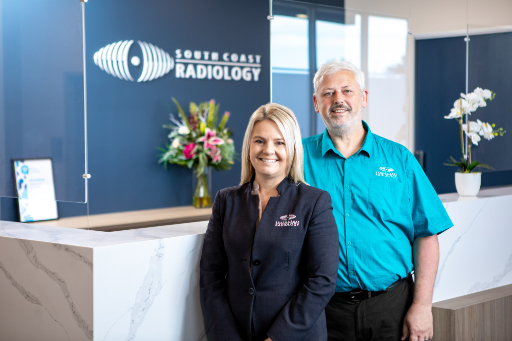 South Coast Radiology Male and Female Staff Members standing facing the camera smiling in the Blue south Coast Radiology Uniform