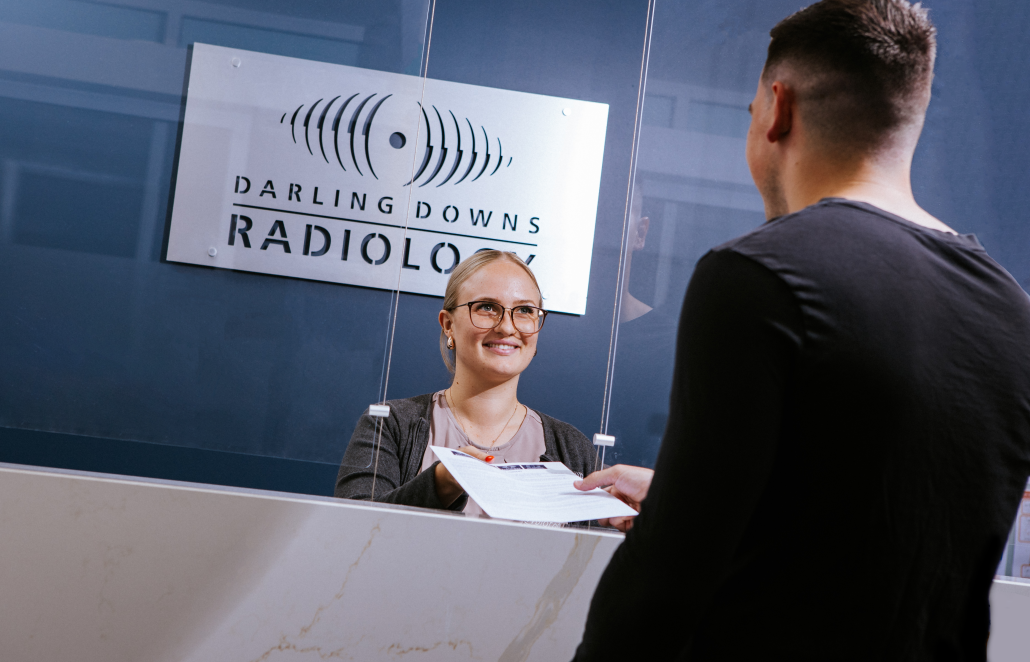 Darling Downs Radiology Receptionist handing over forms to a male patient with their back to the camera